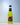 A bottle of Midori Splice cold drink with bright yellow-green liquid, featuring a black and orange label, set against a light blue gradient background.